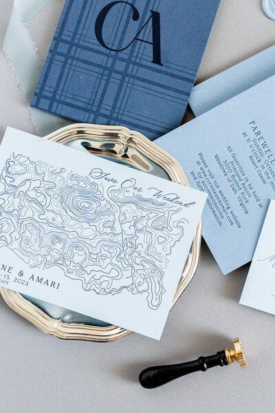 Refined and luxury save the date suite featuring a custom topographic map, soft blue letterpress monogram, classic serif typography, and layered paper goods. Styled with a silver tray, wax seal stamp, and silk ribbon for an editorial, destination-inspired wedding aesthetic.