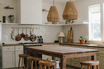 Warm, rustic kitchen with wooden countertops, hanging pots, and woven pendant lights, representing a cozy, nourishing home environment.