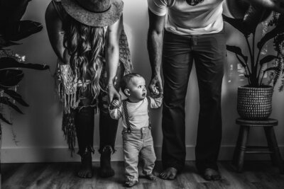 mom and dad holding hands of toddler with suspenders