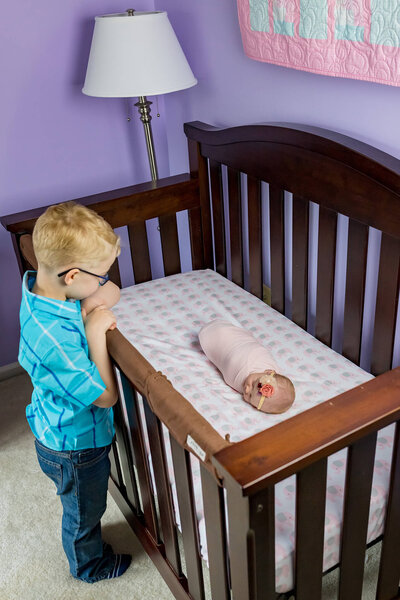 A big brother peaking into his baby sister's crib in Manassas, Virginia.