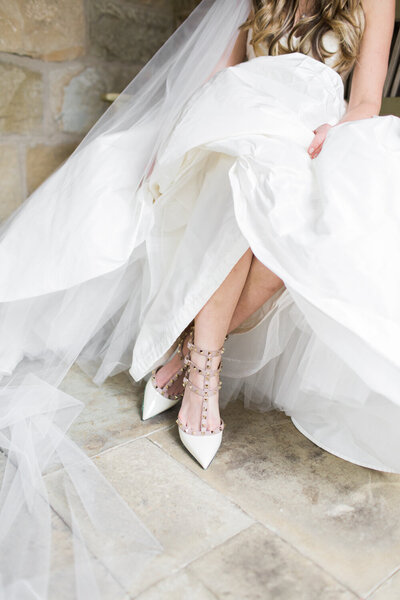 A close-up of a bride’s elegant white gown and statement designer heels, showcasing wedding day fashion and luxury coordination details.