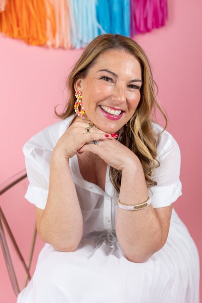 Woman with Dark Hair in white dress sitting with pink background
