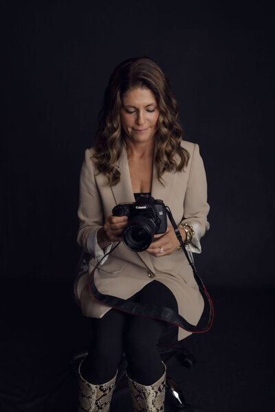 Kerri Link sits in a softly lit studio holding a camera, reflecting her creative eye for beauty, healing, and resilience.