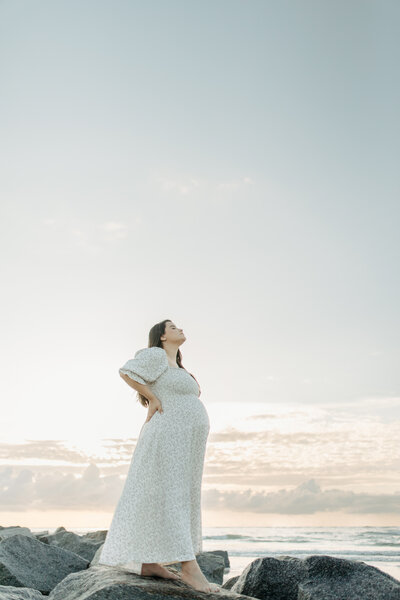 Maternity Portrait taken at Vilano Beach near Jacksonville with the mother in a blue Nothing Fits But dress as she gazes into the sunrise