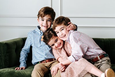 three siblings squeezing each other and laughing in natural light studio