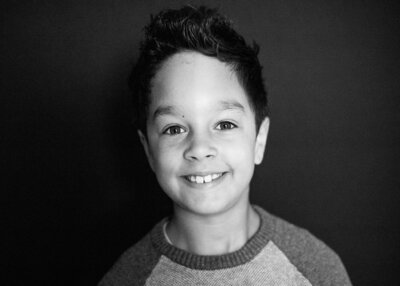 Black and white portrait of grade school boy smiling at camera with black background by Portland School Photography