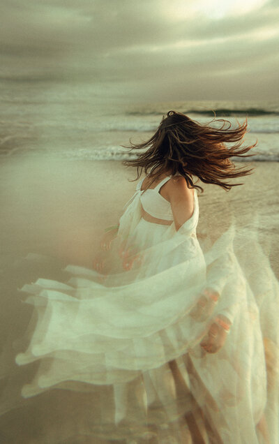 Women twirling around on the beach, hair flowing in the wind, clouds in the sky,