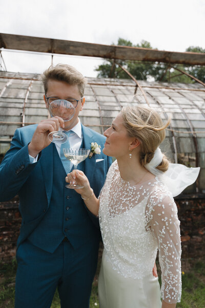 Bruidspaar staat voor glazen serre en drinkt champagne.