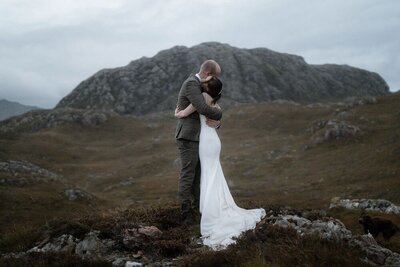 Couple hold each other tight in front of a mountain after their elopement near Torridon, Scotland
