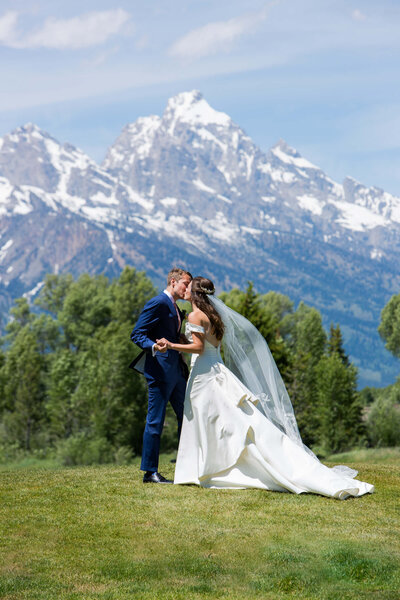 A couple dances on a green hillside at Jackson Hole Golf & Tennis Club, with the Tetons rising behind them. The bride’s flowing veil catches the breeze.