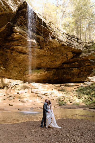 Bride and groom embracing and laughing in front of the waterfall at Ash Cave.