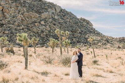 Groom to be holds his wife's stomach from behind during a maternity photo session at Joshua Tree National Park