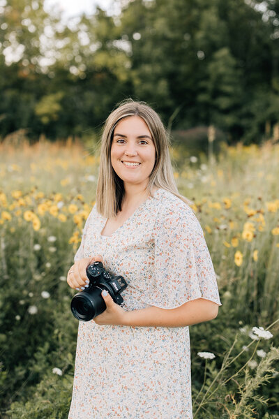 Erin Sage, Metro Detroit and Ann Arbor Area photographer, smiling in a flower field with a camera.