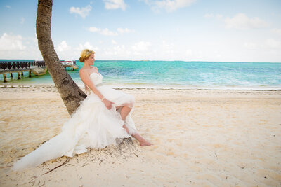 Bride leaning against palm tree on beach