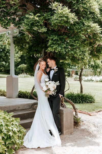 A bride in a white wedding dress standing next to a groom in a green outdoor setting