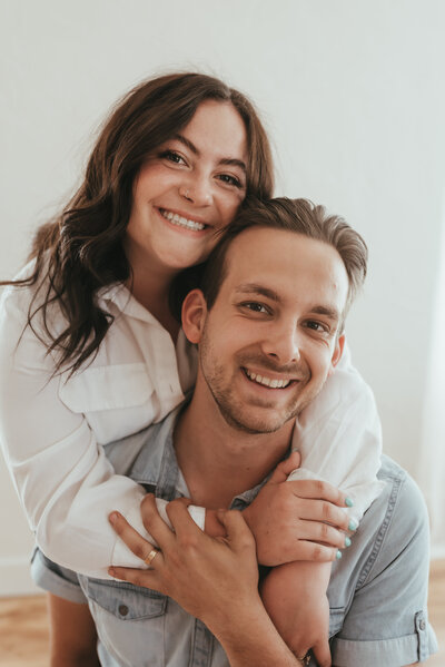 Couple smiling while the woman wraps her arms around the man's neck.