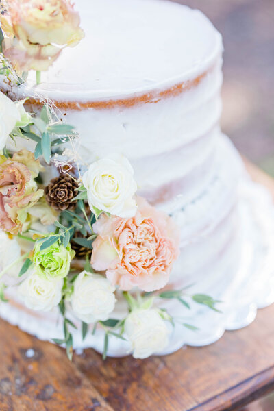 Naked two-tier wedding cake with white icing sitting on brown table with cascade of pink and white carnations and greenery down the left side taken by New Orleans wedding photographer Elizabeth Collins