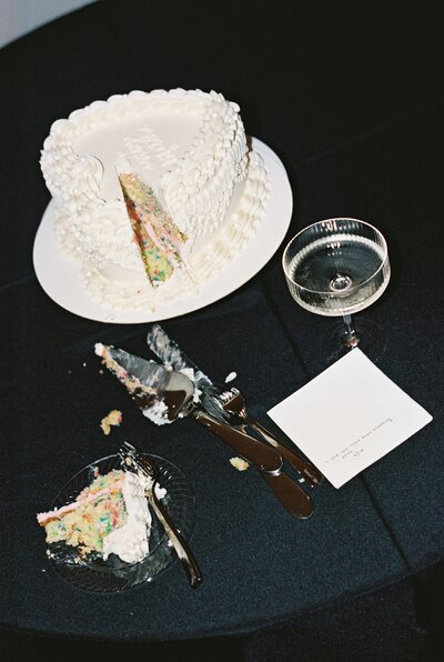 Modern wedding cake cutting moment at The Arlo in Texas. A partially sliced white cake, champagne glass, and cake-cutting utensils sit on a black tablecloth, creating an artistic and editorial wedding reception detail.