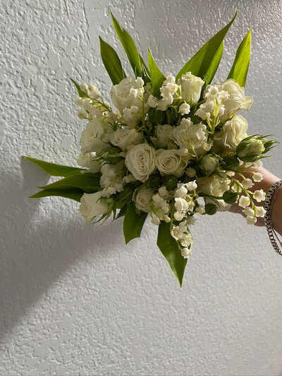 White and green bridal bouquet held against a textured wall