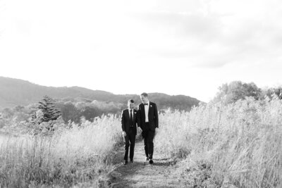 Two grooms walk hand in hand through a North Carolina field