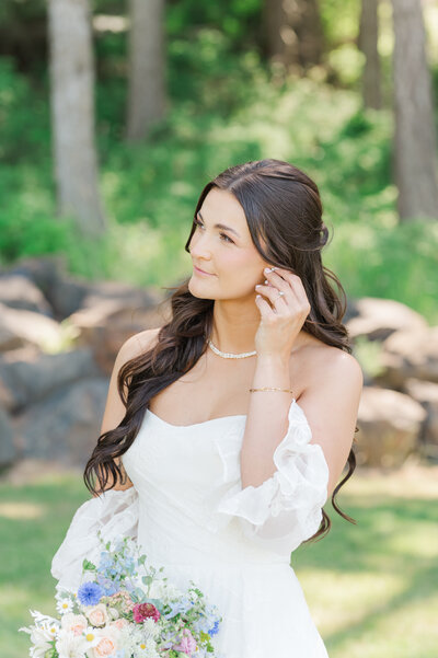 bride in wedding dress playing with earring holding her bouquet at twin creeks farm wedding venue