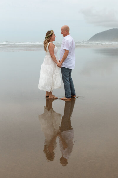 Couple holds hands after their elopement at Canon Beach in Oregon. Their reflection shows in the sand. 