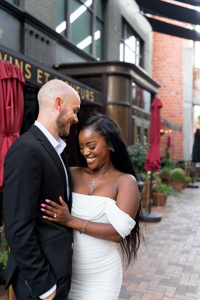 Photographer captures a moment between a couple. They are holding each other and she looks down on the floor. He is gazing at her. 