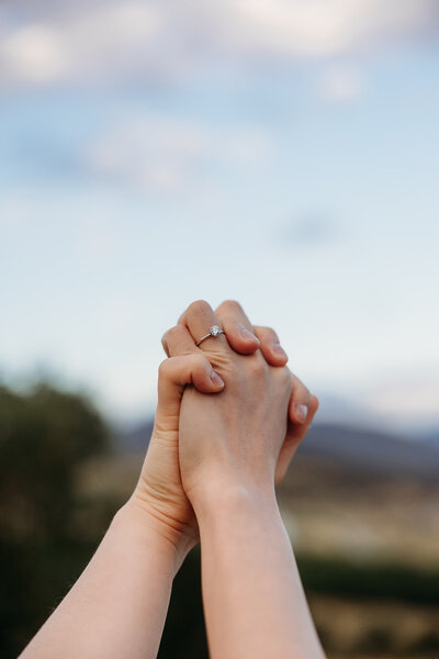Couple holding hands in the air - only hands shown with engagement ring. Photo taken at the National Arboretum Canberra. By Canberra Wedding and Engagement Photographer, Acacia & Grace Photography