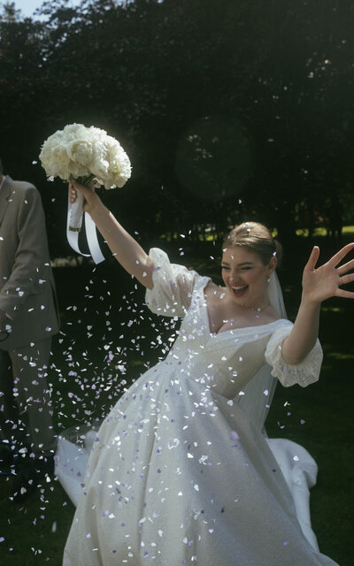 A happy newlywed woman joyfully celebrating with a bouquet of peonies, surrounded by colorful confetti, capturing the excitement of her special day