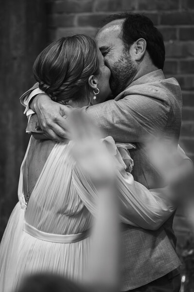 Een intiem zwart-wit moment van een bruid en bruidegom die elkaar liefdevol omhelzen tijdens hun trouwceremonie.