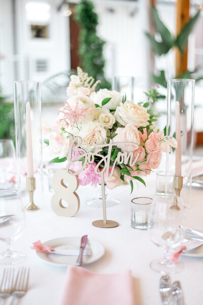 A beautifully styled reception table at The Bohlin featuring soft pink and ivory florals, taper candles, and a modern “Boston” table name sign — perfect for a nautical yet romantic wedding.