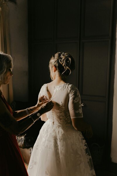 Older woman helping bride button up her lace wedding gown