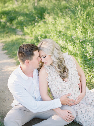 Expectant mother and father snuggling on the ground on beautiful summer evening