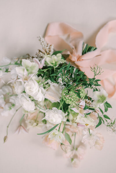 A film inspired photo of a wedding bouquet of pink and white roses with a pink ribbon