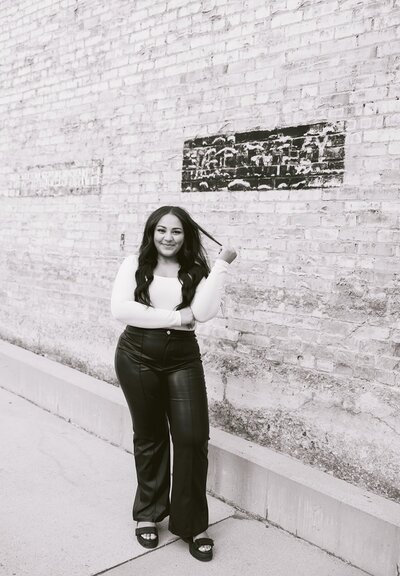 Black and white, Women standing in front of brick wall, Black pants, black shoes, white top, Holding hair in hands