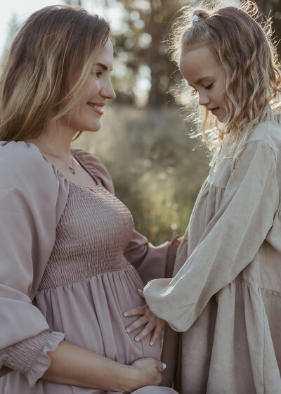 Pregnant mother watching her little girl touch her pregnant belly for their maternity photography session