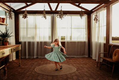 Young girl dancing in a sun filled brick greenhouse  on a jute rug
