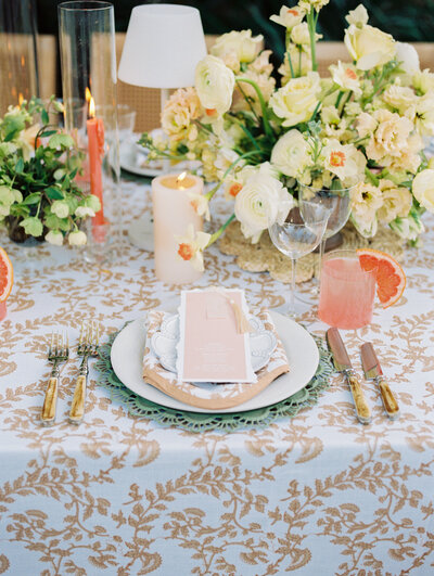 peach tablescape with white and green flowers, a grapefruit drink, and a gold leaf patterned tablecloth