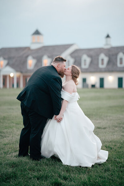 Newlyweds holding hands and kissing on a lawn 