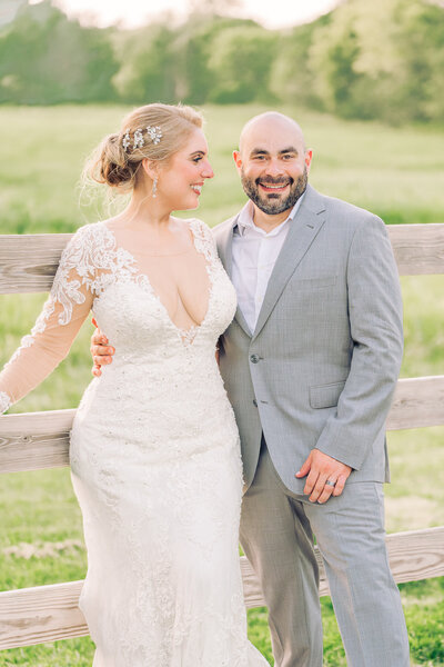 A smiling newly wed couple next to a fence at sunset in the Raleigh countryside at the end of their wedding reception celebrating their destination wedding photography