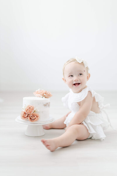 one year old girl at first birthday smash cake photoshoot with bambinos cookies naked cake decorated with pink roses