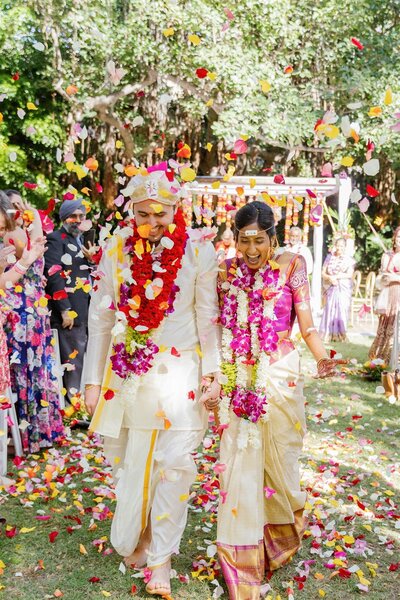 A newlywed couple walking back up the aisle as guests shower them with colorful flower petals 