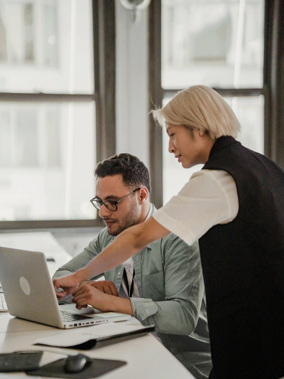 Woman explaining something to a man on his Macbook