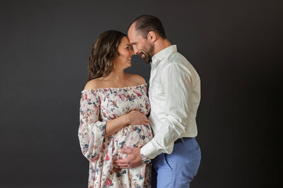 A couple hugging mom's pregnant belly and touching foreheads.