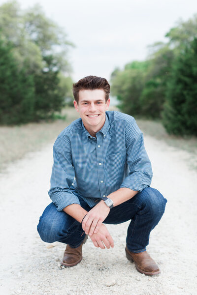 Senior portrait of guy kneeling in casual pose on trail in Malibu