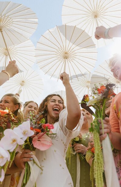 Joyful bridal party with colorful flowers and white parasols at a Boulder, Colorado wedding. A heartfelt moment showcasing timeless artistry and vibrant wedding celebrations.