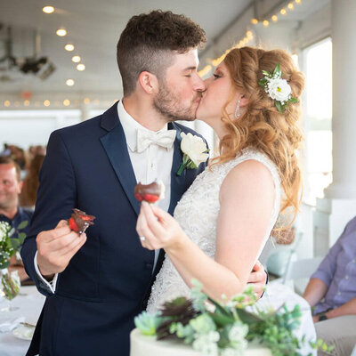 bride and groom kiss while holding strawberries at receoption
