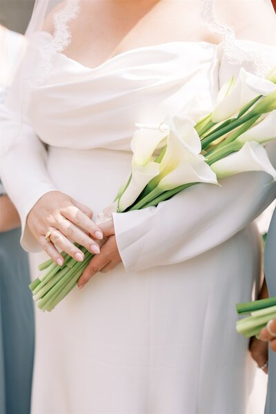 A close up of a brides bouquet in her arms, made up of only calla lilies.