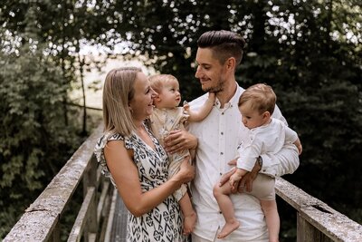 Mutter und Vater stehen auf einer Bruecke und haben zwei Kinder auf dem Arm