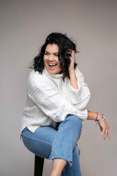 Gig Harbor mom and Author Angie Garner Laughing in a white sweater and jeans, sitting with a gray background